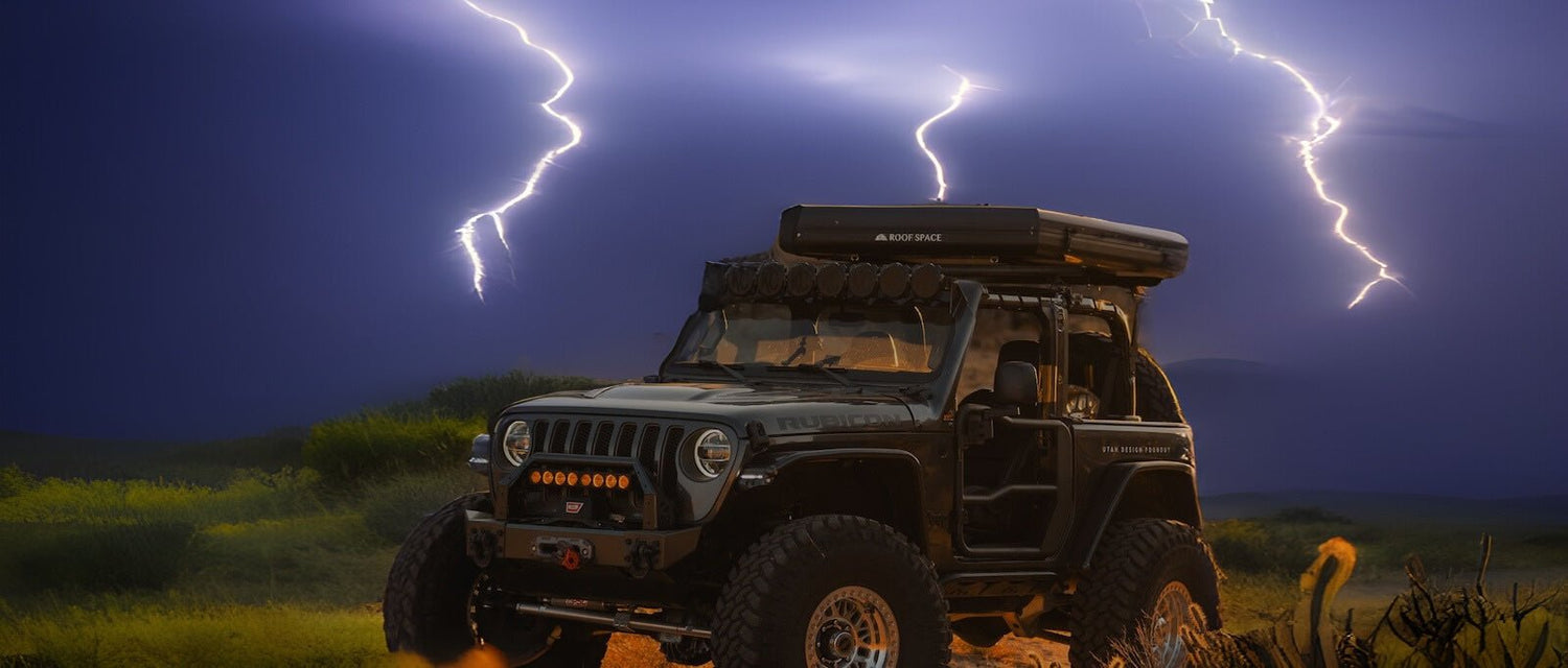 Ein schwarzer Jeep Rubicon mit Dachzelt steht inmitten eines Gewitters; Blitze erhellen dramatisch den Nachthimmel.