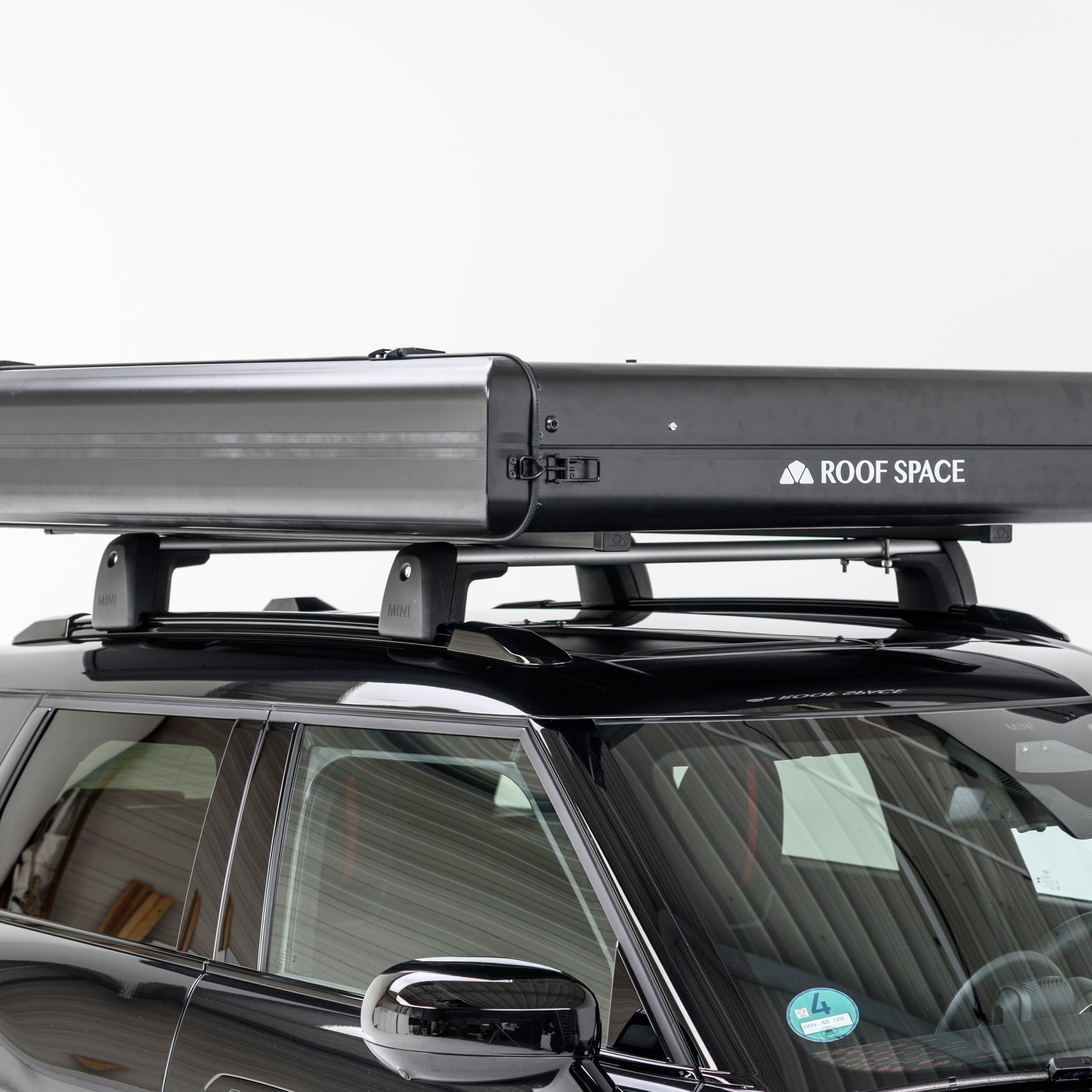 Ein schwarzer Mini Cooper mit einem schwarzen Dachgepäckträger von Roof Space vor einem weißen Hintergrund. Der Träger ist mittig platziert.