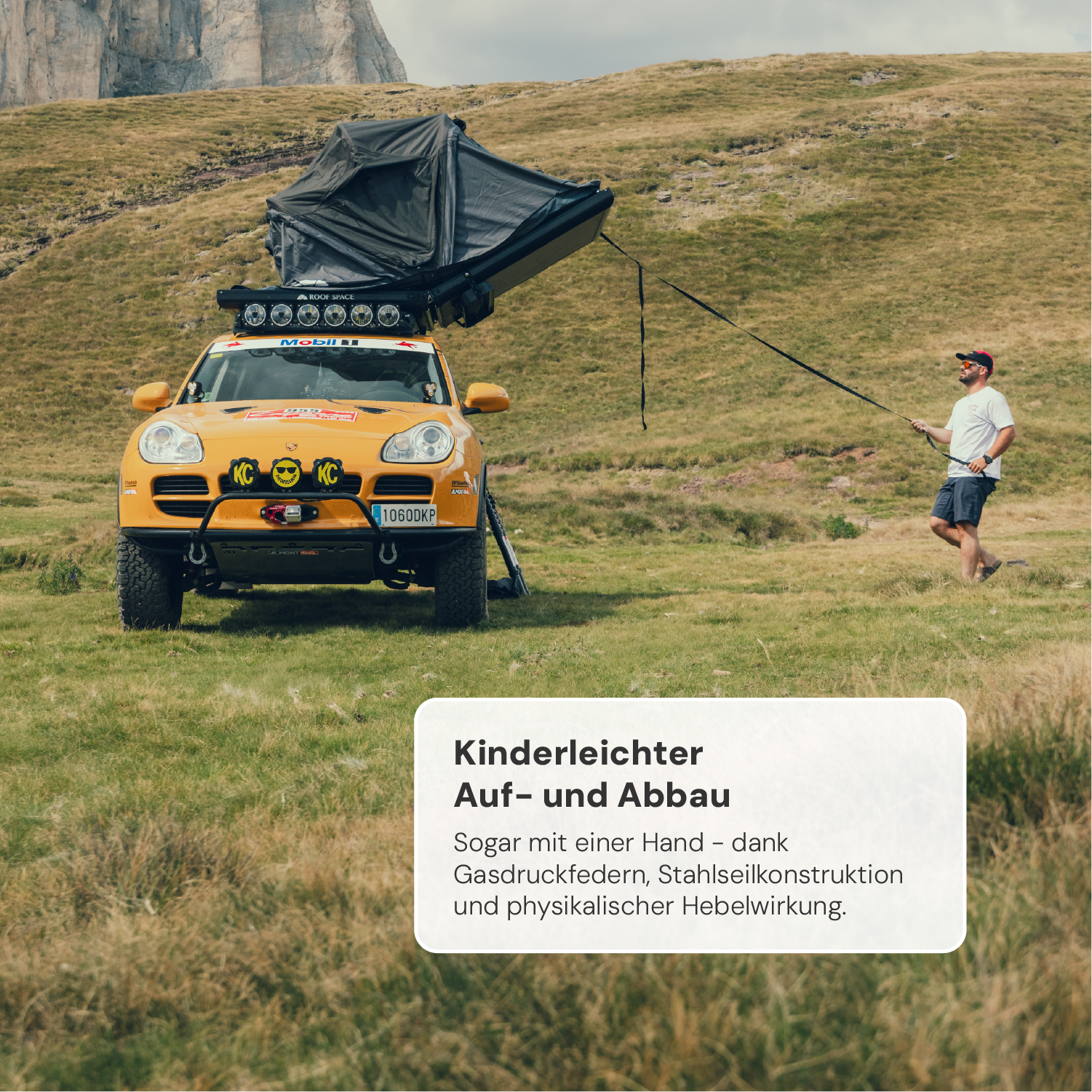 Gelber Porsche Cayenne mit Dachzelt in hügeliger Landschaft, Mann zieht Seil, Textfeld: "Kinderleichter Auf- und Abbau", "Mobil", "KC", Kennzeichen "1060DKP".