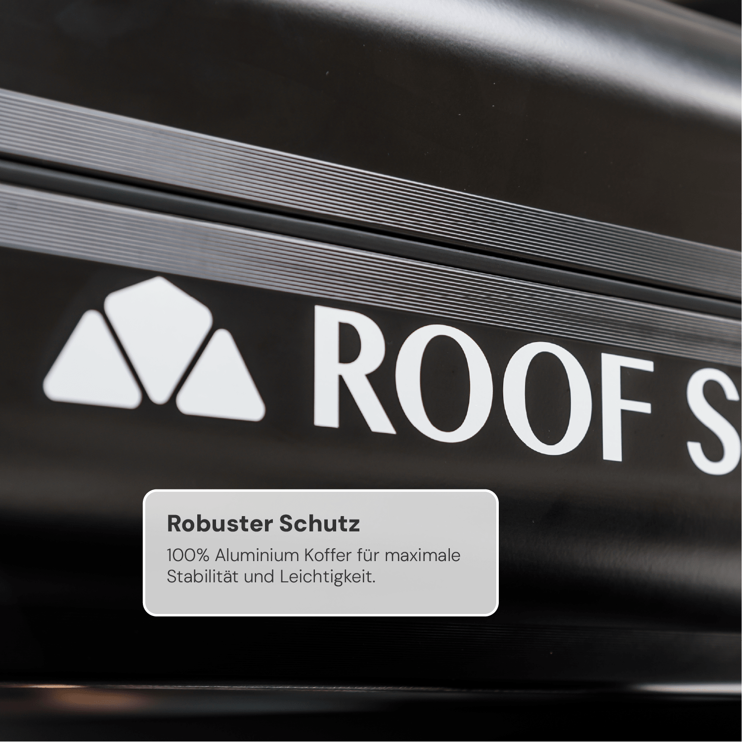 Nahaufnahme eines schwarzen Aluminium-Dachkoffers mit weißem Logo und Text "Roof". Darunter steht "Robuster Schutz: 100% Aluminium Koffer für maximale Stabilität und Leichtigkeit."