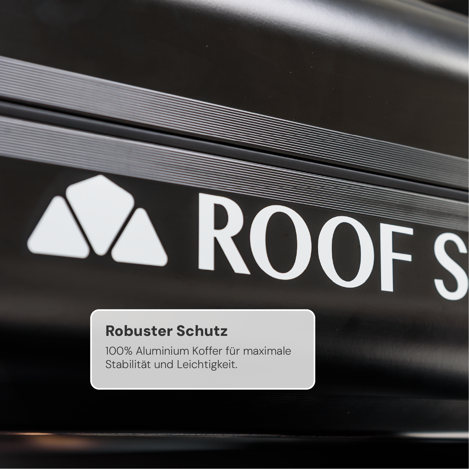 Nahaufnahme eines schwarzen Aluminium-Dachkoffers mit weißem Logo und Text "Roof". Darunter steht "Robuster Schutz: 100% Aluminium Koffer für maximale Stabilität und Leichtigkeit."