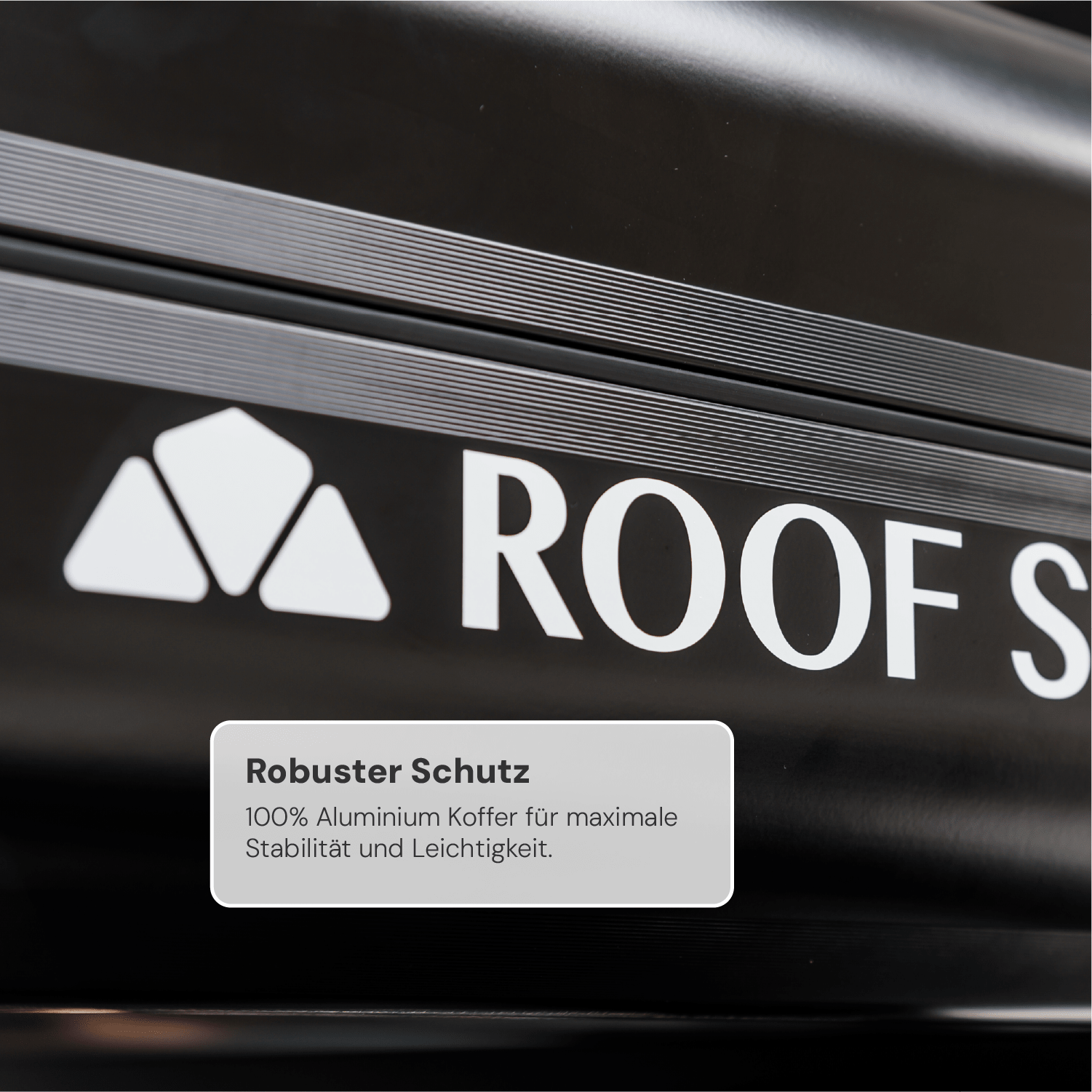 Nahaufnahme eines schwarzen Dachkoffers mit weißem Logo „ROOF S“ und Text „Robuster Schutz. 100% Aluminium Koffer“.