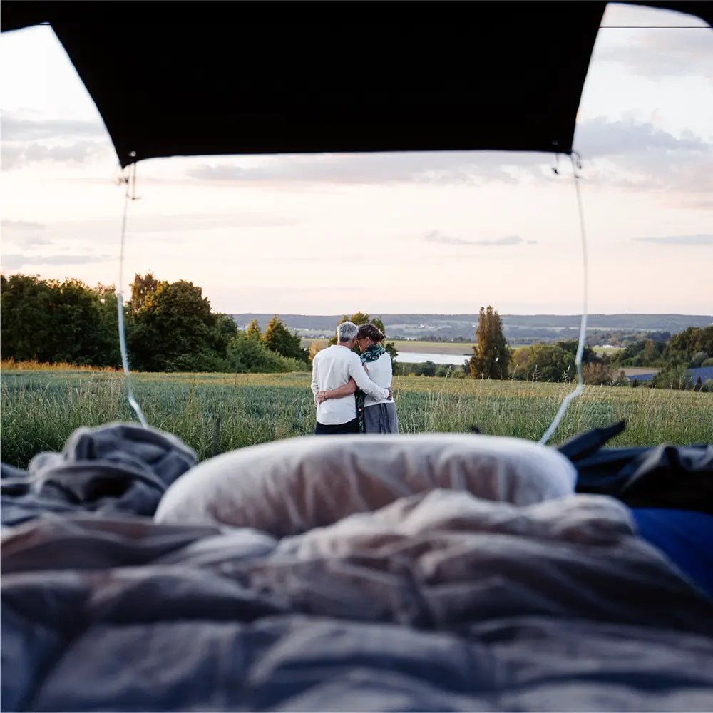 A couple in front of the Roof Space 4 rooftent, enjoying the scenic view over a meadow.