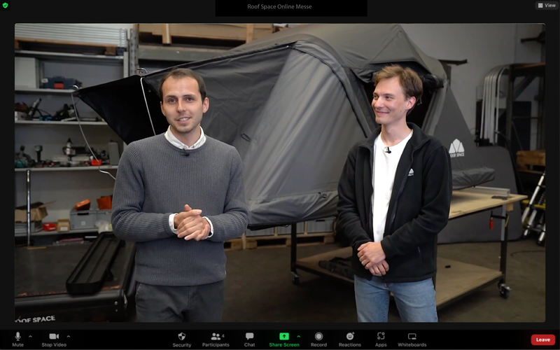 Zwei Männer vor einem grauen Dachzelt auf einer Online-Messe, der linke Mann trägt einen grauen Pullover, der rechte eine schwarze Jacke. Text: "Roof Space Online Messe", "OF SPACE".