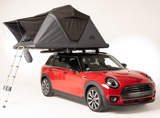 Rotes Mini Cooper mit montiertem, grauem Dachzelt und Leiter. Urlaubstimmung pur mit sicherer Dachzeltbefestigung.