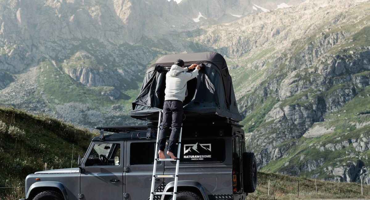 Graues Auto mit Dachzelt vor alpiner Bergkulisse. Camping-Lifestyle für Abenteuer und unvergessliche Momente in der Natur.
