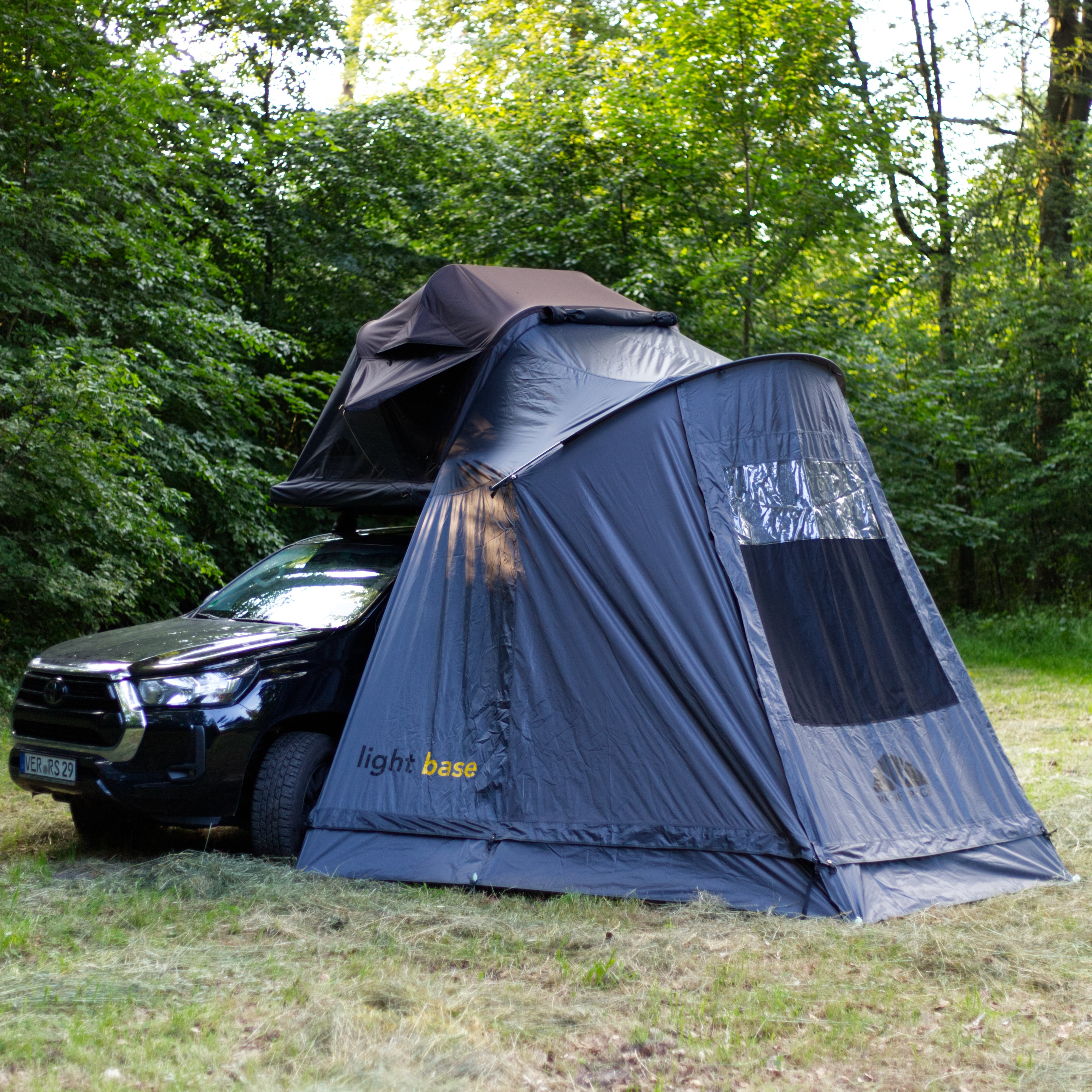 Schwarzer Geländewagen mit Dachzelt und Vorzelt im Grünen. Abenteuerlustige Campingausrüstung für nachhaltige Outdoor-Erlebnisse.

