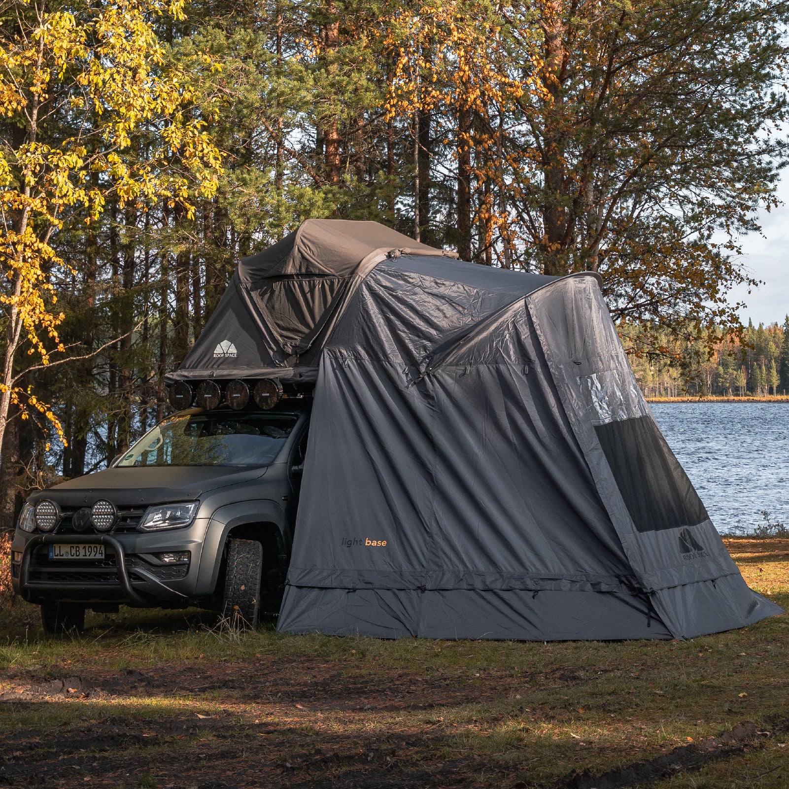 Das Light Base Vorzelt ist in einer malerischen Naturkulisse zwischen Wald und See aufgebaut und bietet zusätzlichen Wohnraum neben dem Geländewagen.