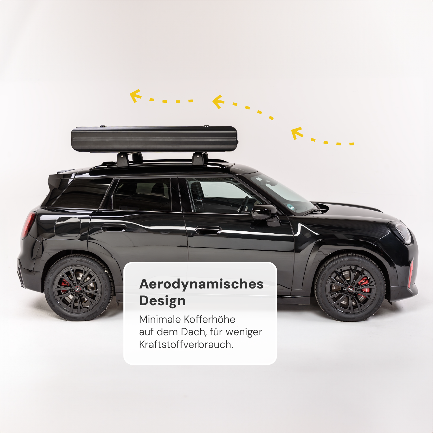 Schwarzes Auto mit schwarzer Dachbox auf weißem Hintergrund, gelbe Pfeile deuten auf Aerodynamik. Text: "Aerodynamisches Design. Minimale Kofferhöhe [...] Kraftstoffverbrauch."
