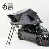 Schwarzer Mini Countryman mit Dachzelt und Leiter auf weißem Hintergrund. Das Zelt ist grau und trägt das "German Design Award Winner 2024"-Logo.