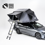 Graues Auto mit Dachzelt und Leiter vor hellem Hintergrund. Text oben links: "GERMAN INNOVATION AWARD '25 WINNER".