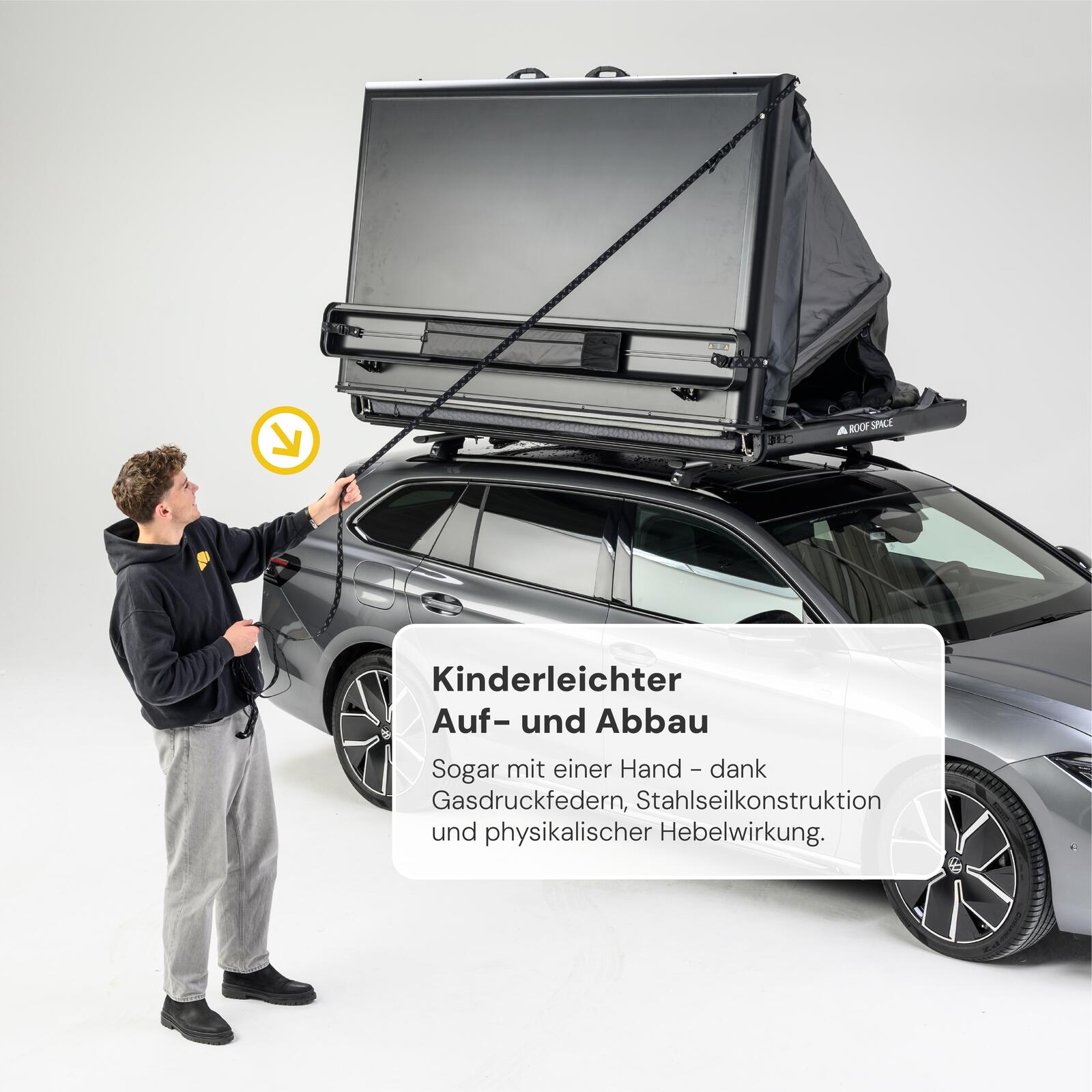 Ein junger Mann öffnet ein graues Dachzelt auf einem grauen Auto mit einem Seil. Text: "Kinderleichter Auf- und Abbau."