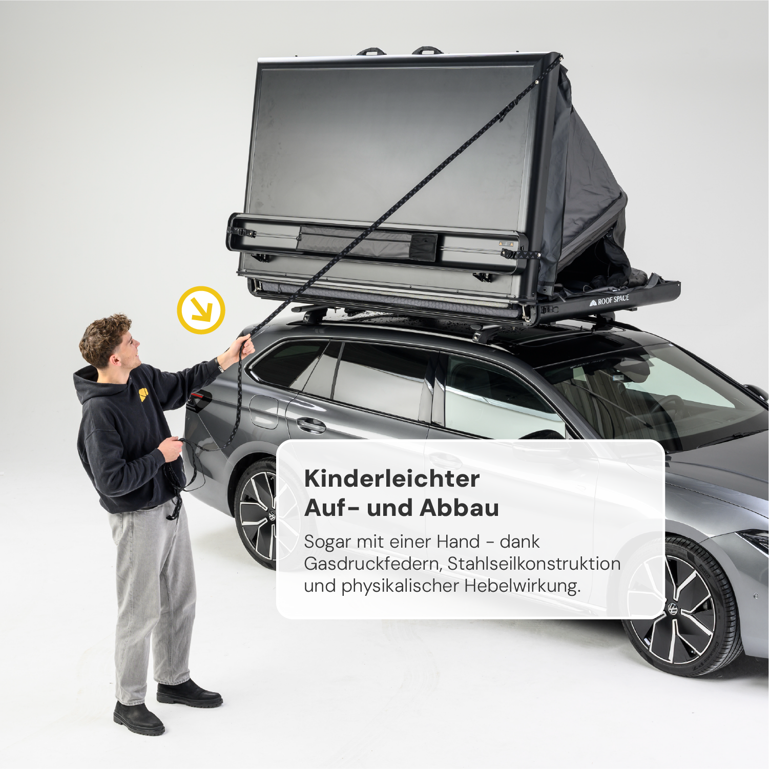 Ein junger Mann öffnet ein graues Dachzelt auf einem grauen Auto mit einem Seil. Text: "Kinderleichter Auf- und Abbau."
