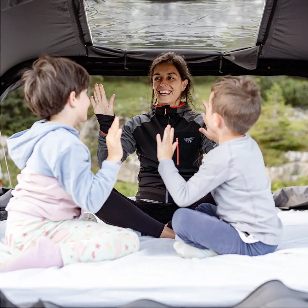 A mother and two children smiling and high-fiving inside the cozy rooftop tent Roof Space 4 with the open panoramic window with nature in the background