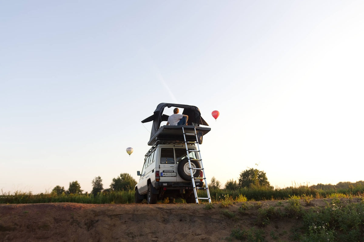 Dachzelt auf einem Auto mit Heißluftballons im Hintergrund.